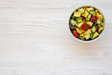 Obraz na płótnie Canvas Fresh Avocado Tomato Salad in a bowl on a white wooden background, top view. Flat lay, overhead, from above. Space for text.