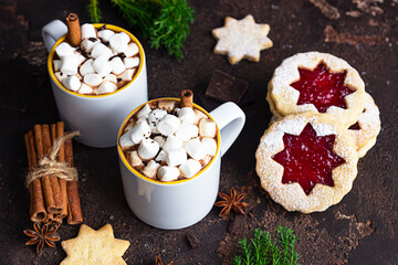 Two cups of hot chocolate or cocoa with marshmallow and cinnamon stick, bitter chocolate, winter spices and jam filling cookies. Festive Christmas or New Year decoration. Dark background.