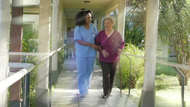 Light rays warming hospital scene. Elderly woman helped by african female doctor in the garden