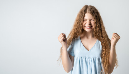 Joyful girl keeps fists clenched and exclaims in triumph, celebrates success. Studio shot white background. Copy space