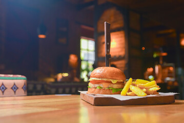Delicious juicy chef cheeseburger served with fries on a rustic wooden board on a table in bar or restaurant.