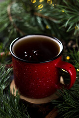 New year's tea party with spices. Red mug with tea surrounded by garlands, fir branches and spices	
