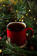 New year's tea party with spices. Red mug with tea surrounded by garlands, fir branches and spices	
