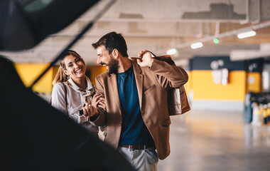 Young attractive fashionable couple walking towards their car and attending to put shopping bags into a trunk.