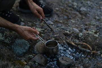 Ground black coffee in a copper Turk is brewed and boils on camp fire.