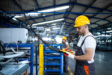 Factory worker wearing uniform and hardhat operating industrial machine with push button joystick in production hall. Employee working on industry production machine.