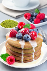 Matcha pancakes served with condensed milk, blueberry and raspberry on white plate, vertical