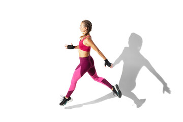 Fototapeta na wymiar Running. Beautiful young female athlete practicing on white studio background, portrait with shadows. Sportive fit model in motion and action. Body building, healthy lifestyle, style concept.