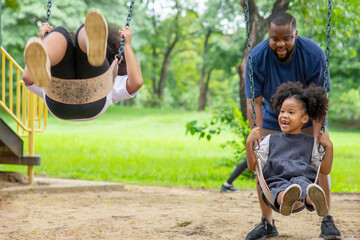 Happy affectionate mixed race family. African man father with two little daughter playing swing...