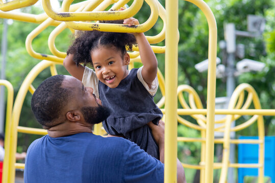 Happy Affectionate Mixed Race Family. African Man Father Carrying Little Daughter Playing At Playground In The Park. Dad And Cute Child Girl Enjoy And Having Fun Together In Outdoor Weekend Vacation.