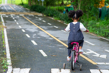 Happy affectionate mixed race family. Rear view of little cute child girl riding bicycle alone in the park. Adorable girl enjoy and having fun learning ride a bike in outdoor weekend vacation