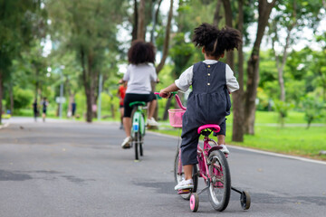 Happy affectionate mixed race family. Two little cute child girl sister  riding bicycle together in the park. Adorable sibling enjoy and having fun learning ride a bike in outdoor weekend vacation.