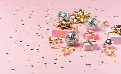 Gold and silver decorations, mirror disco balls, gifts on pastel pink paper background.