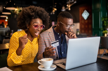 Attractive smiling african couple sitting in cafe and purchasing over internet things for house.
