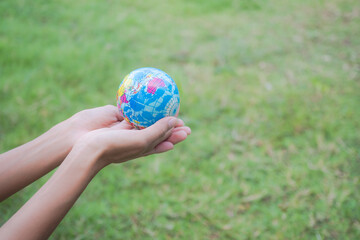 Close up hand woman holding earth on blur image of grass background. Environmental conservation Earth Day concept. copy space.