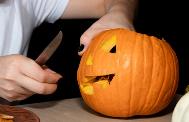 A man holds a knife with his hands, carves a face in a pumpkin on the eve of a Halloween party.