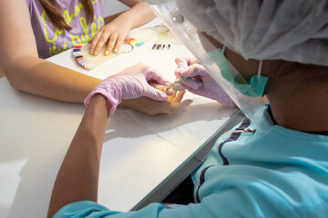 A master in a protective screen, mask and pink gloves cuts off the old nail Polish from the client's nails in the process of hardware manicure.