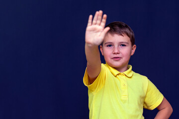 Little 9s boy putting his hand out making stop sign gesture.Blue studio wall