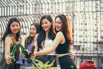 Group of Asian girl having party with hand holding beer bottle toasting at outdoor restaurant. drinking alcohol, young people night lifestyle. positive emotion and friendship concept. copy space