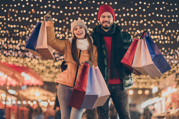 Black friday. Photo of two people friends raise buy shopping bags under x-mas christmas outdoors evening lights wear winter outerwear