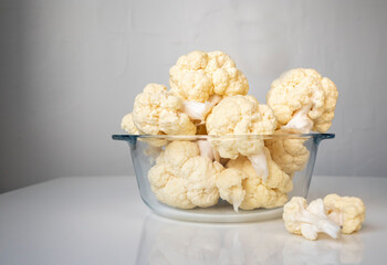 Fresh cauliflower in a glass saucepan on a white table. Side view.