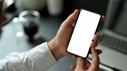 Male hands holding mock up smartphone while sitting at worktable