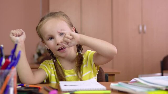 A beautiful little girl sits at the table and counts her fingers on her hand. Preschool education. 4k