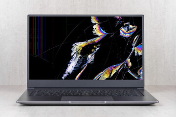 laptop with a broken screen in color spots and cracks on a gray background close up front view