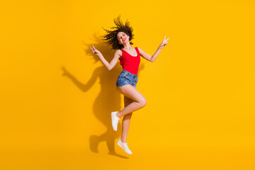 Fototapeta na wymiar Full length body size view of her she nice attractive slim fit cheerful cheery optimistic wavy-haired girl jumping having fun showing v-sign isolated bright vivid shine vibrant yellow color background