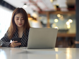 Portrait of female office worker working with laptop and smartphone on office desk