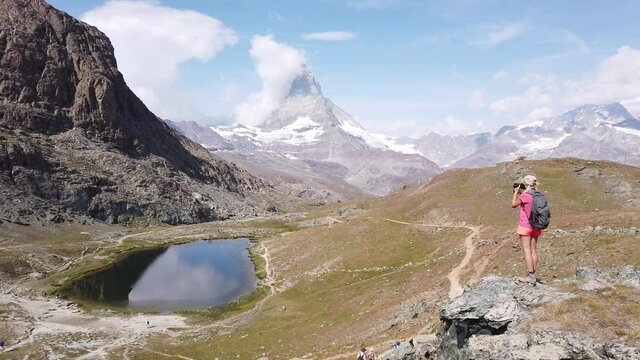 Tourist woman photographer at Mount Matterhorn and Swiss Alps reflected on Riffelsee Lake. On riffelseeweg trail by Gornergrat Bahn cog railway. Tourism in Zermatt, Canton of Valais, Switzerland.