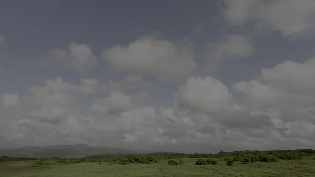 Amazing daytime timelapse video of countryside region during rainy season, with dramatically drifting white cloud balls in clear blue sky background and mountain range at horizon. Natural phenomenon.