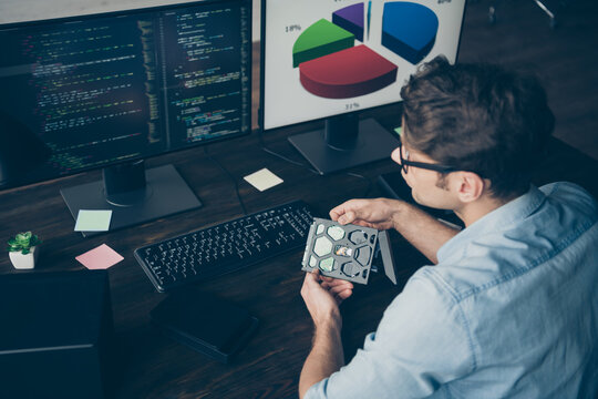 High angle view back rear spine photo of focused it specialist guy engineering sit desk look screen monitor pc hold disc analyze testing operating system in workplace workstation