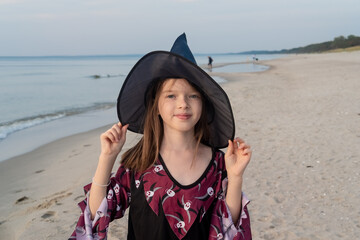 girl in a hat and witch costume celebrating halloween on the beach