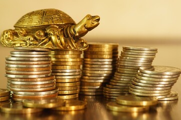 A metal turtle next to a stack of coins. Symbol of financial well-being.