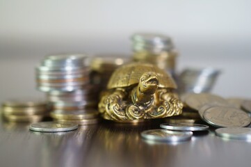 A metal turtle next to a stack of coins. Symbol of financial well-being.