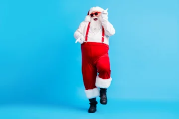 Poster Foto in voller Größe von funky Fat Crazy Santa Claus mit großem Bauch Bart Tanz Weihnachten Stechpalme Party Club tragen Hosenträger Overalls Sonnenbrille Stiefel isoliert blauer Hintergrund © deagreez