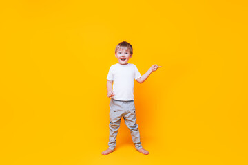 Fototapeta na wymiar Cute boy on yellow background points with his hand to the side, photo for advertising product