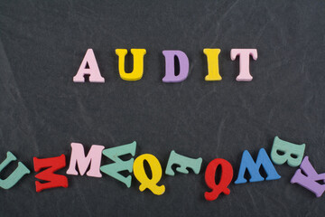 AUDIT word on black board background composed from colorful abc alphabet block wooden letters, copy space for ad text. Learning english concept.