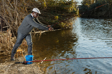 Portrait of positive African man standing with fishing rod near river