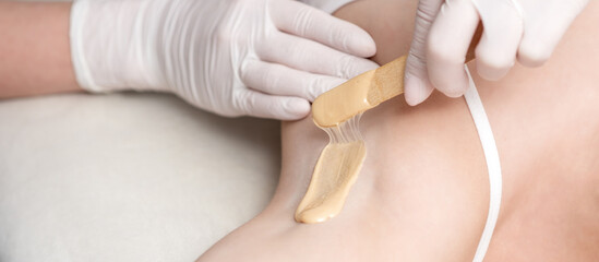 Depilation and epilation female armpit with liquid sugar paste by spatula. Hand of cosmetologist applying wax paste on armpit. Smooth underarm concept