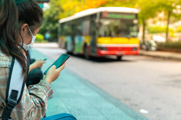 Asian young girl use smartphone waiting for bus at bus stop