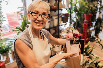 Senior female florist working in her flower shop and prepares online orders using laptop.
