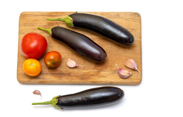 Three eggplants, tomatoes and cloves of garlic on a wooden kitchen board on a white background. Ingredient for fitting a dietary vegetable dish.