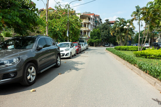 Parallel cars parking on street with green trees