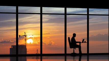 Fototapeta na wymiar The businessman sitting near a panoramic window against the city sunset