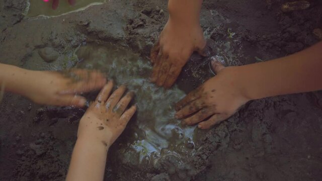 Hands of two little girls splashing water and making a swimming pool out of a mud puddle as a part of their play with water during the hot summer afternoon