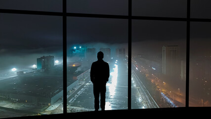Fototapeta na wymiar The man standing near the panoramic window on the foggy city background