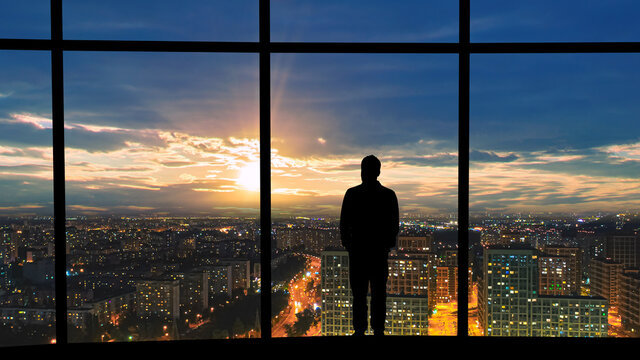 The male standing near the panoramic window against the beautiful sunset