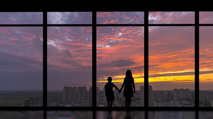 Fototapeta na wymiar The boy and girl standing near the panoramic window on the sunset background